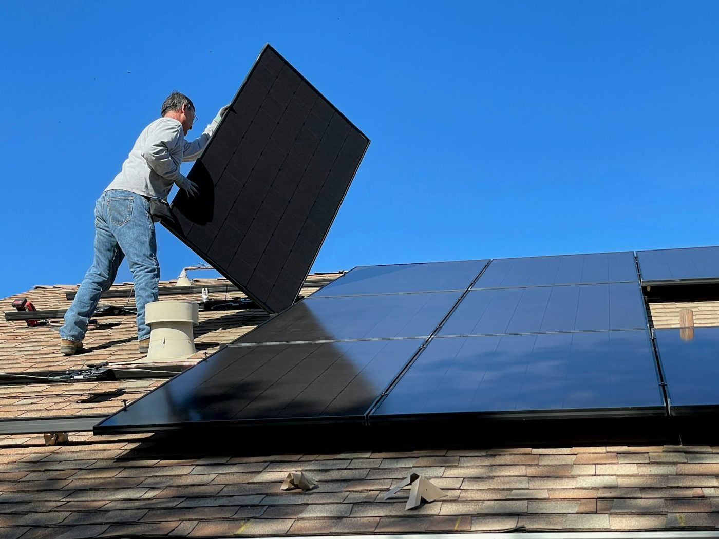 Illustrative photograph of a technician placing a solar panel on a roof. This person is not identified as Maspro Energy staff, and this is not a Maspro project.