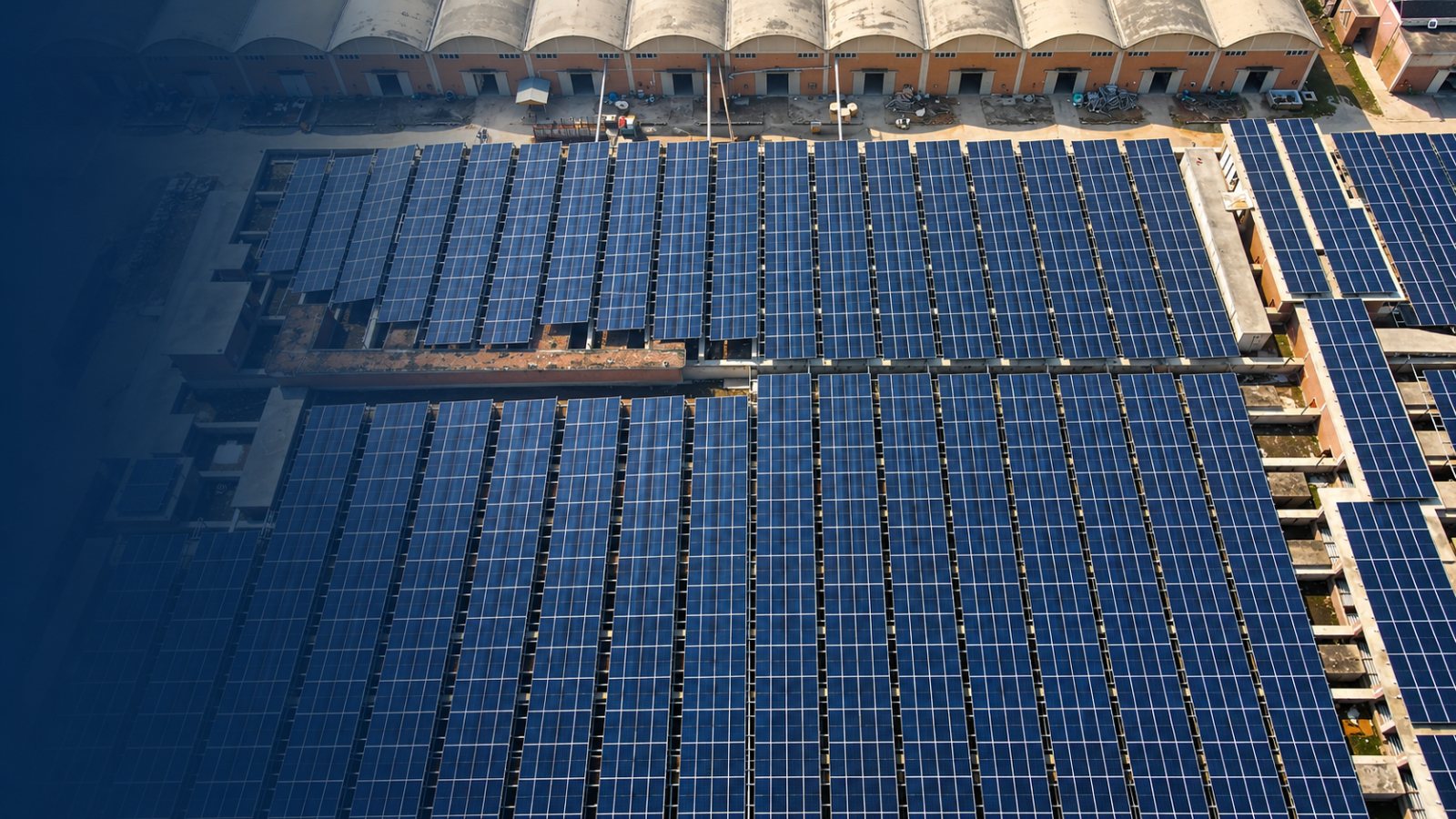 Rows of solar panels installed across an industrial rooftop beside long factory buildings.
